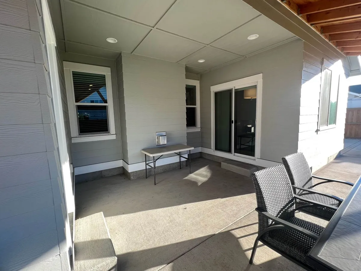 An outdoor patio area featuring a table and chairs set by a sliding door, ideal for dining, working outside, or relaxing. The space is sunlit and inviting for casual gatherings or solo unwinding.