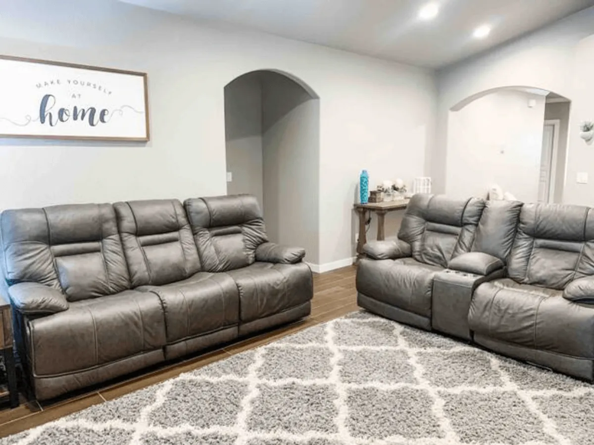 A secondary view of the living space with modern gray leather sofas, a decorative wall sign, and a textured area rug. This perspective emphasizes the open-concept layout and additional comfortable seating for relaxing or socializing.