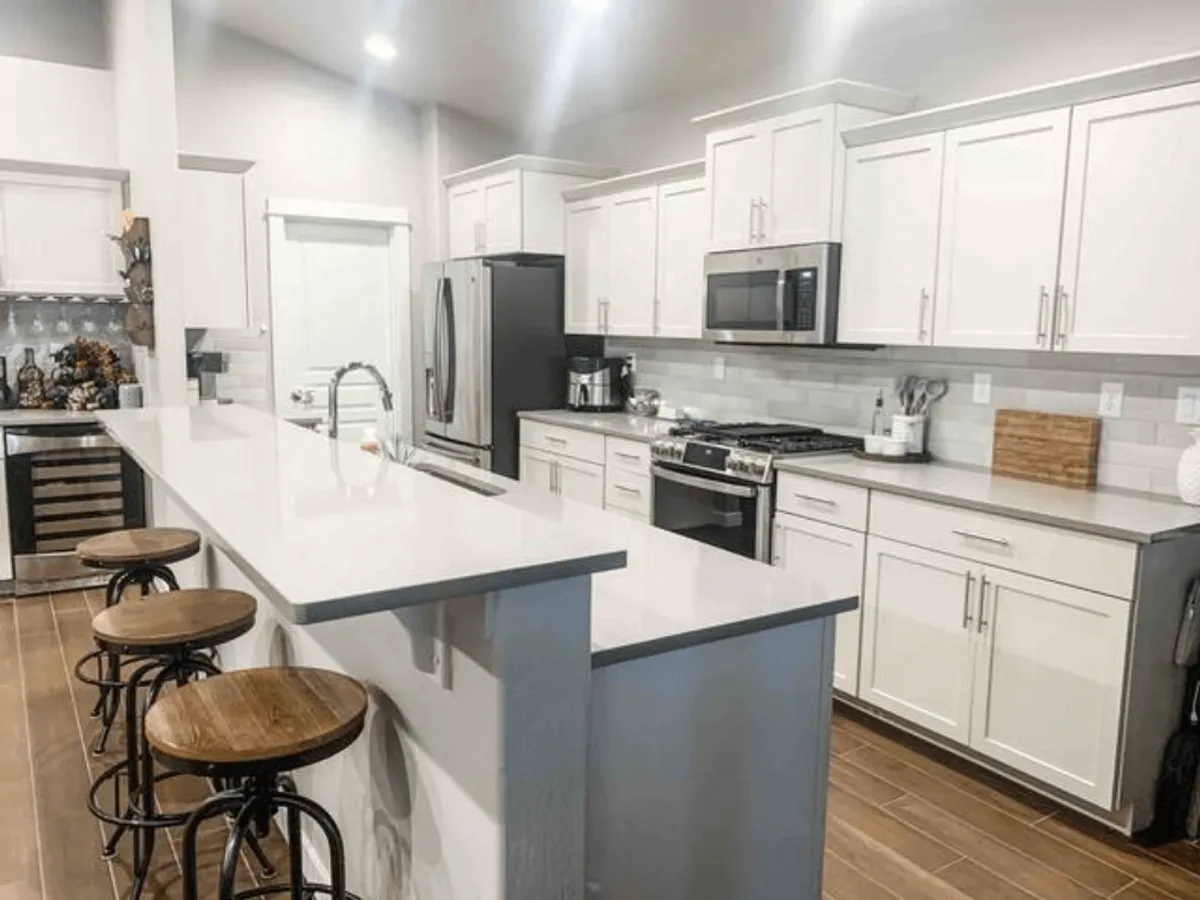 A bright, spacious kitchen with a central island, bar stools, stainless steel appliances, and sleek white cabinetry. The layout is open and designed for both cooking and socializing, with plenty of counter space for meal prep and gatherings.