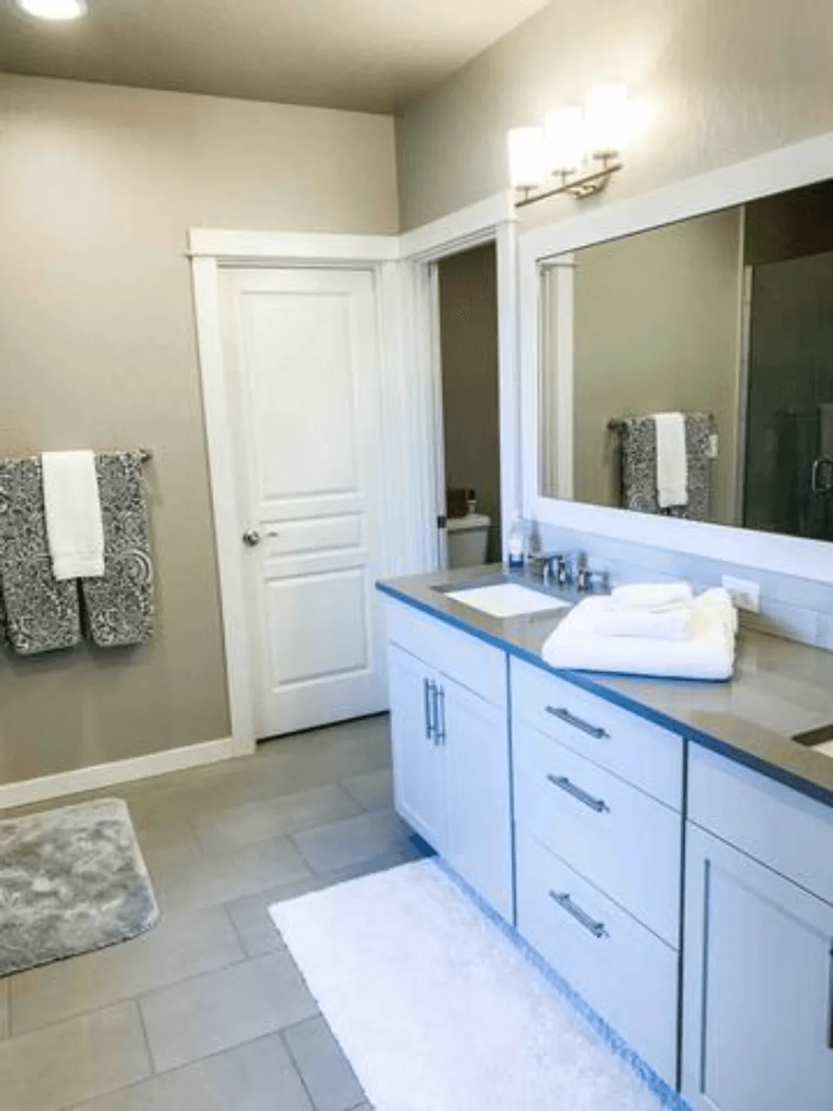 A bright, fresh bathroom with a vanity and sink, large mirror, neatly arranged towels, and a decorative rug, suggesting a spa-like experience and convenience for morning and evening routines.