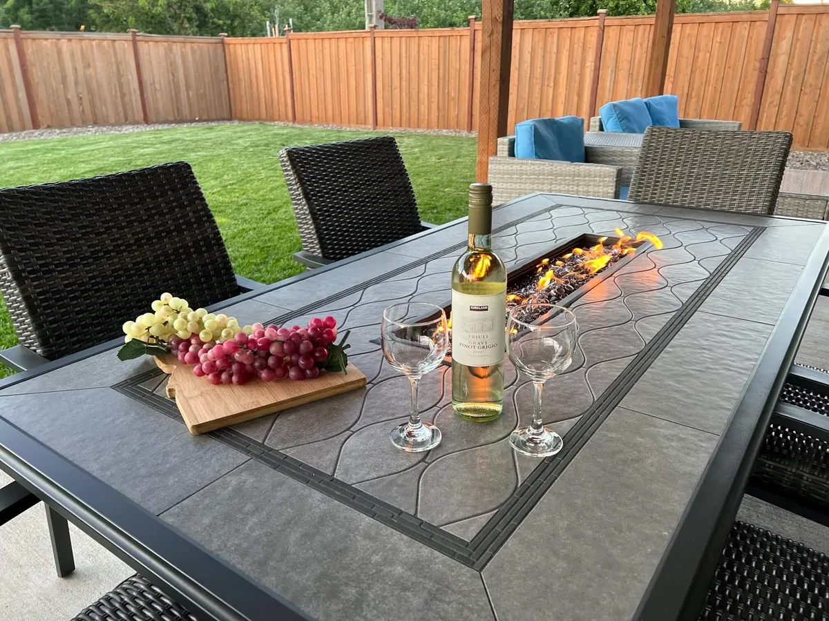 The image showcases an inviting outdoor dining area featuring a cozy fire pit, a table set with wine and glasses, fresh grapes, and a welcoming atmosphere perfect for relaxing or entertaining. The scene radiates warmth and togetherness, emphasizing the home's potential for memorable gatherings.