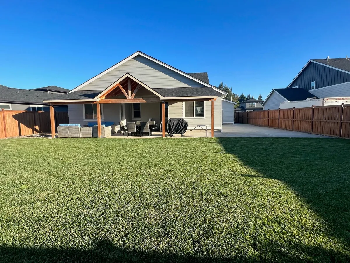 This photo captures a well-arranged covered patio overlooking a grassy lawn. The patio features outdoor seating and a grill, inviting guests to relax, dine, or enjoy a barbecue together. The open view to the backyard allows for easy supervision of children and seamless indoor-outdoor entertaining.