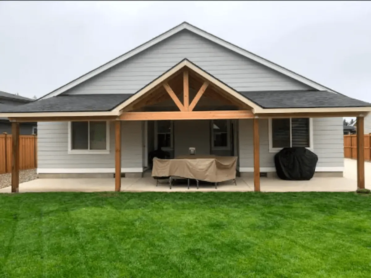 A covered patio overlooking a green lawn, with sturdy wooden posts and the home’s exterior in view. The patio is set up for outdoor dining and relaxation, creating a comfortable space for family gatherings and evening activities.