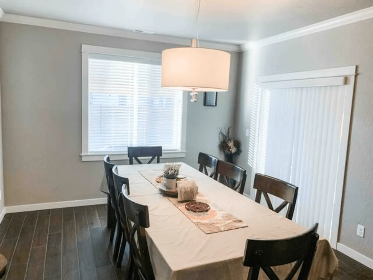 A sophisticated yet family-friendly dining area featuring a large table, elegant chandelier, and a window with blinds letting in soft daylight. The setup is perfect for group meals, celebrations, and intimate family gatherings.