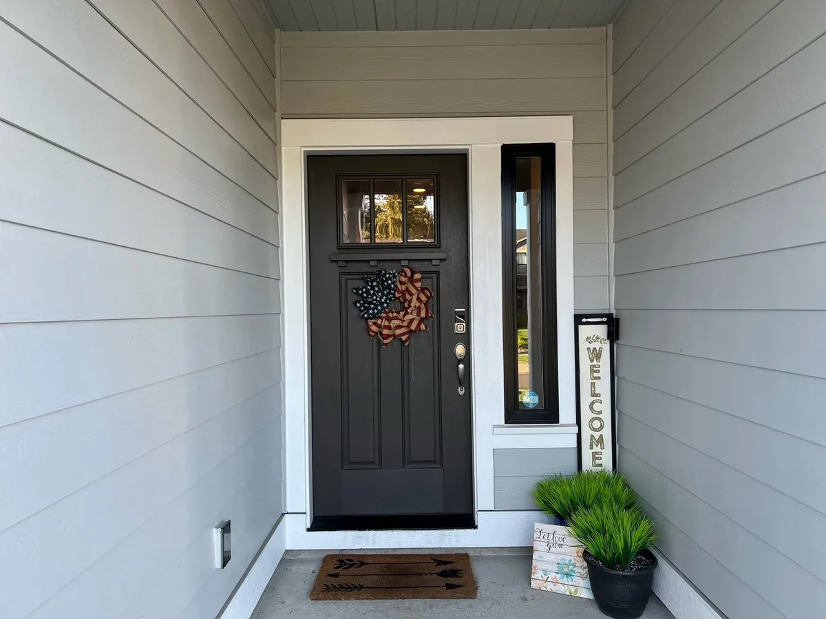 A view of the home's front door, adorned with a welcoming sign, decorative wreath, and potted plant. The porch area is inviting and suggests a pleasant entry experience.
